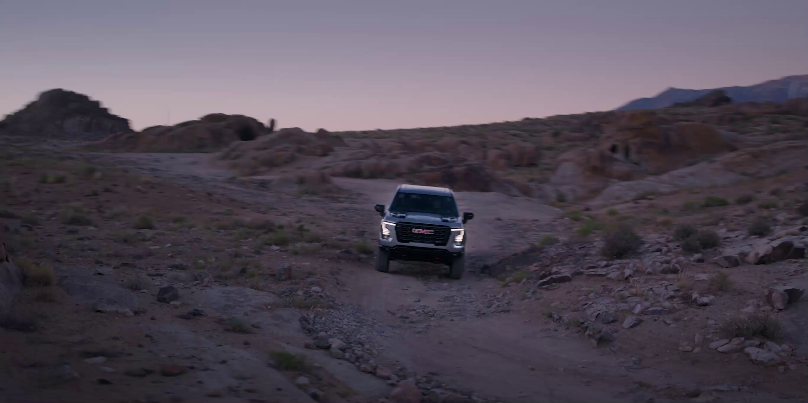 2027 GMC Sierra 1500 driving on a rocky desert trail at dusk